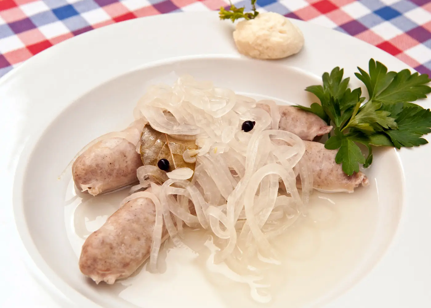 Fränkische Blaue Zipfel mit Zwiebeln und Sud auf einem weißen Teller serviert.